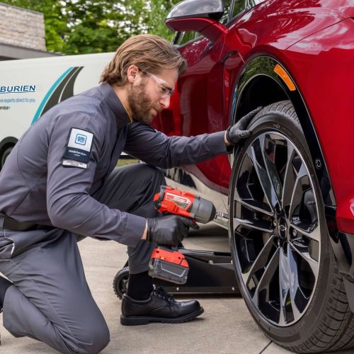 Burien Chevrolet Mobile Service technician using an impact wrench to change a tire on a red Chevrolet SUV
